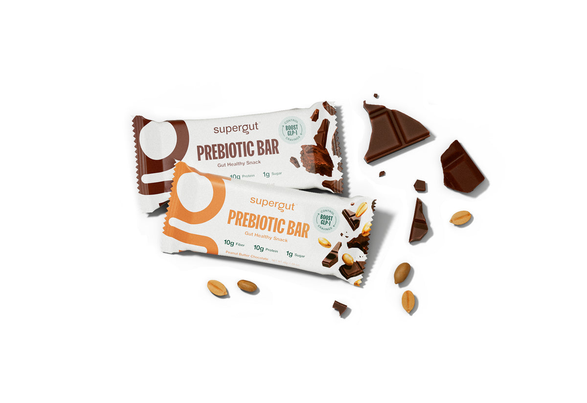 Two wrapped prebiotic bars from the brand 'supergut' on a clean white background, styled with chocolate chunks and almonds scattered around them.